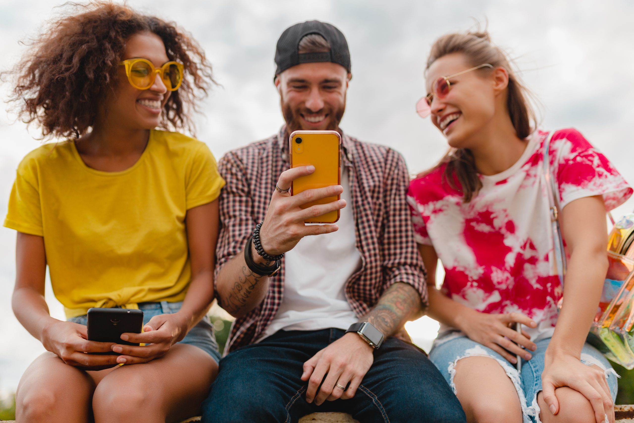 happy young company of smiling friends sitting park using smartphones, man and women having fun together, colorful summer hipster fashion style, communication wireless connecting devices