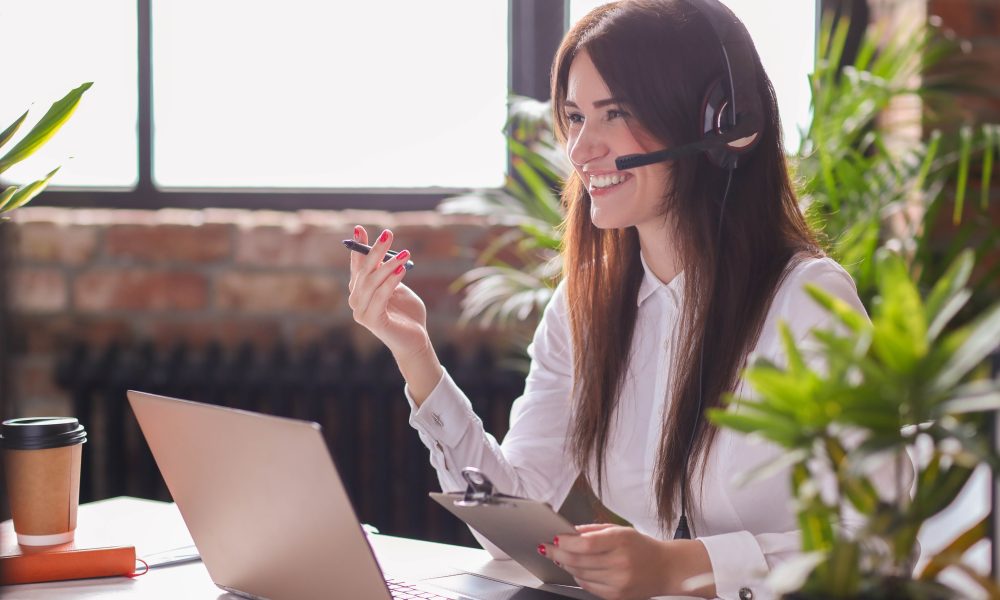 Mulher sorridente realizando o atendimento de um cliente via telefone em uma empresa