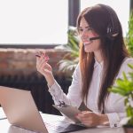 Mulher sorridente realizando o atendimento de um cliente via telefone em uma empresa