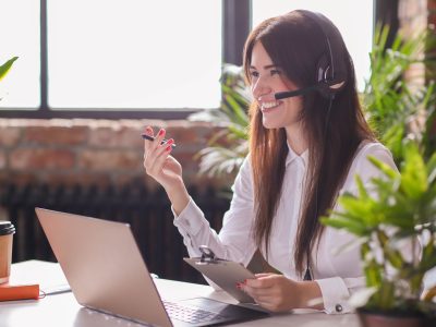 Mulher sorridente realizando o atendimento de um cliente via telefone em uma empresa