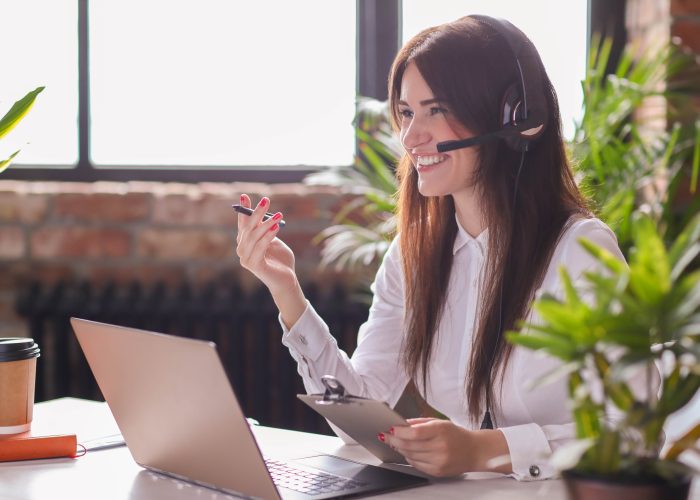 Mulher sorridente realizando o atendimento de um cliente via telefone em uma empresa