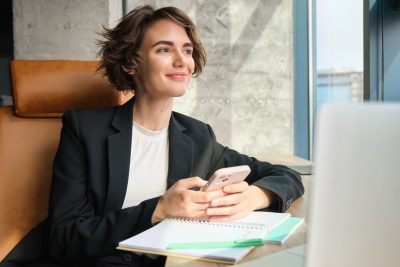 Mulher sorrindo utilizando o celular em um ambiente corporativo