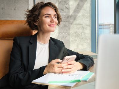 Mulher sorrindo utilizando o celular em um ambiente corporativo