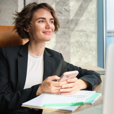 Mulher sorrindo utilizando o celular em um ambiente corporativo